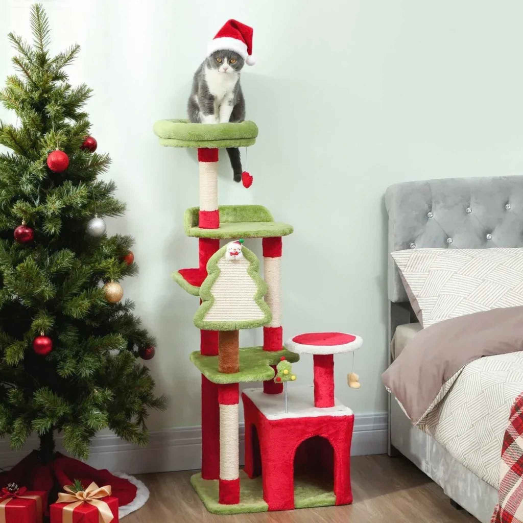 Cat in Santa hat sitting on top of Christmas cat tree next to Xmas tree and presents