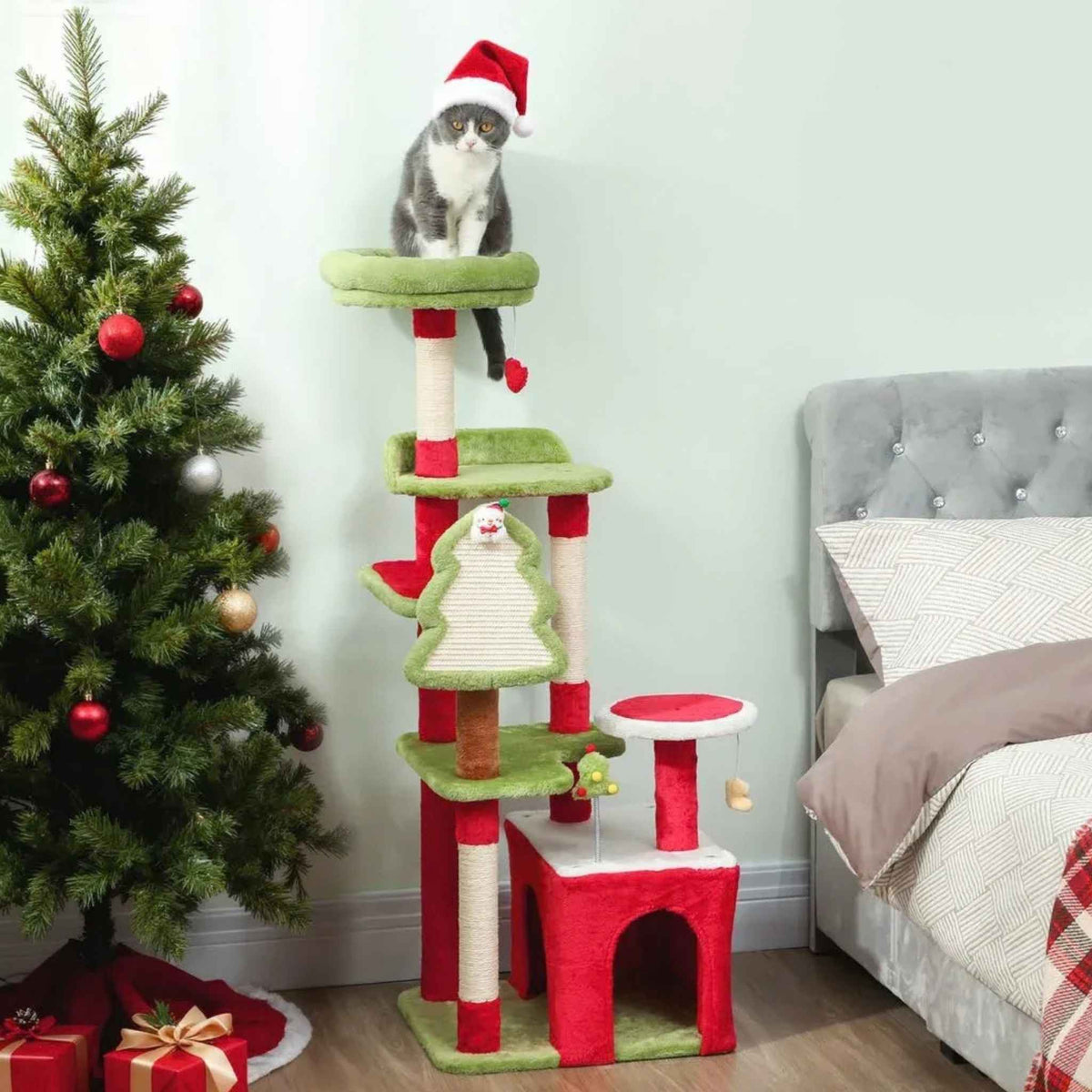 Cat in Santa hat sitting on top of Christmas cat tree next to Xmas tree and presents
