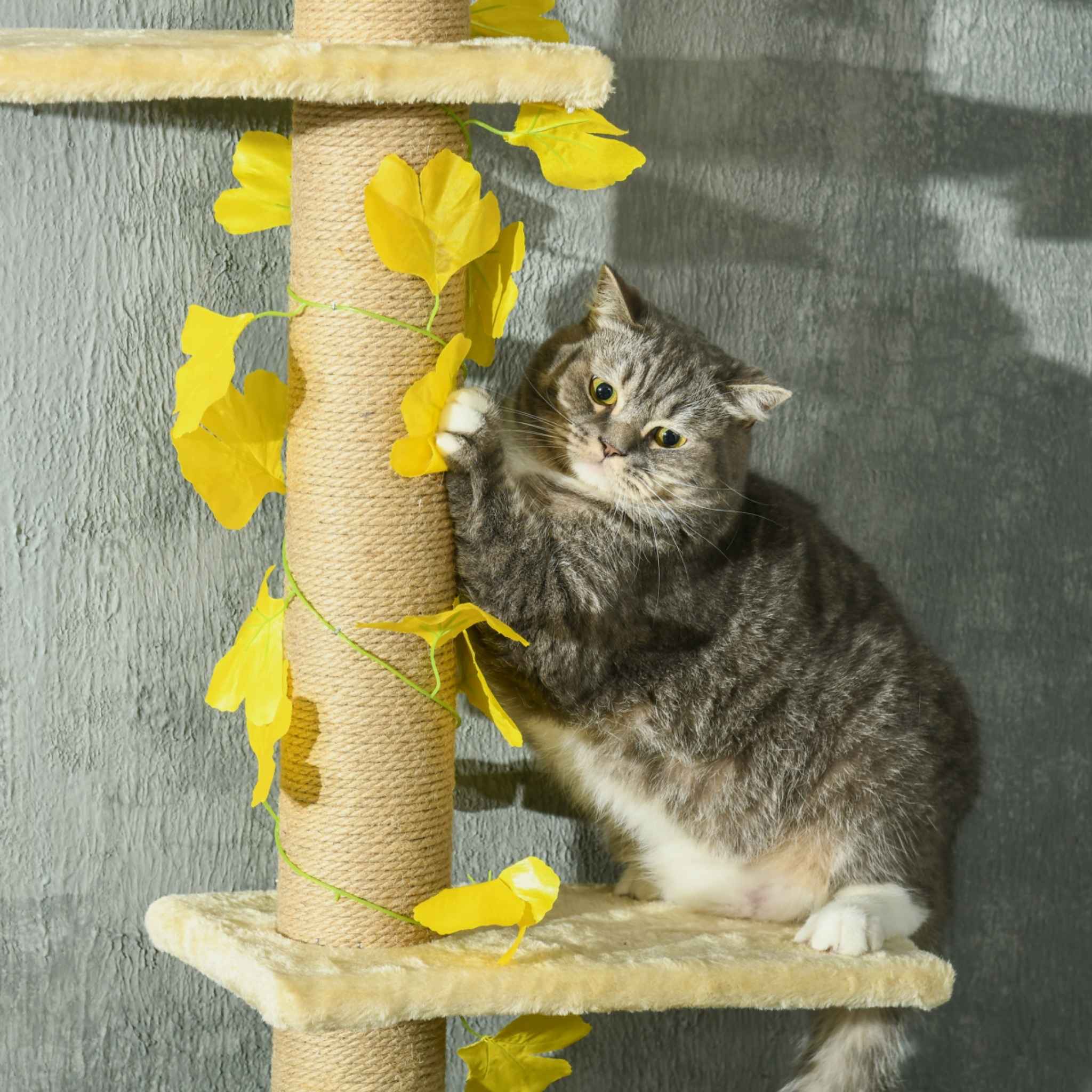 Cat scratching jute rope post on floor-to-ceiling cat tree with leaves