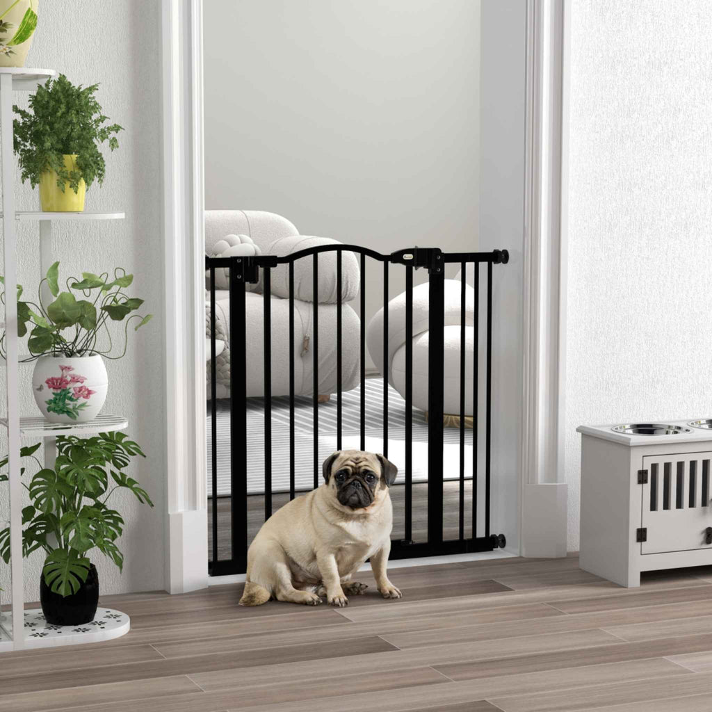 Pug standing in front of black dog safety gate