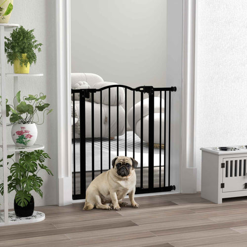 Pug standing in front of black dog safety gate