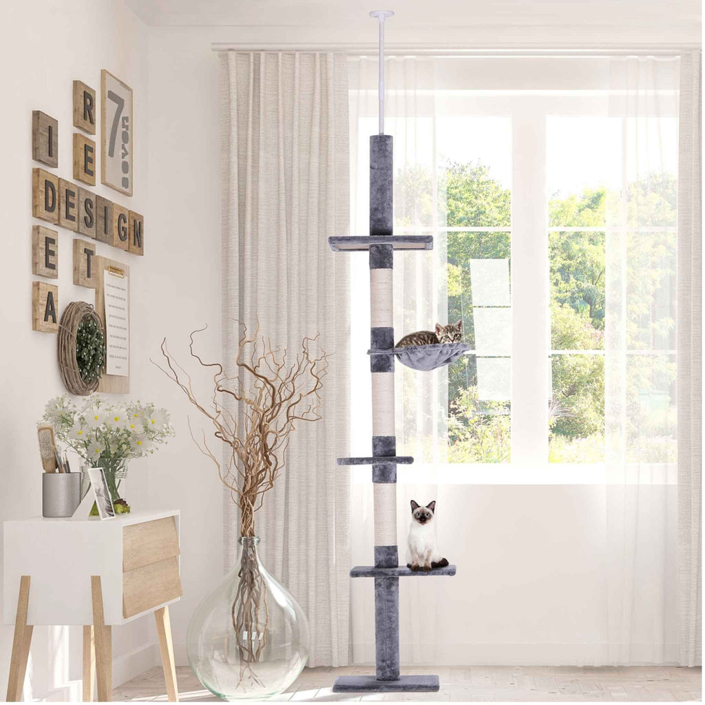 Two cats sitting on floor to ceiling cat tree in living room
