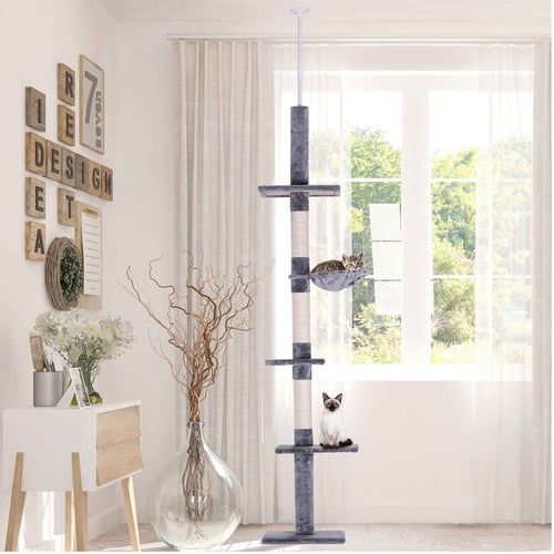 Two cats sitting on floor to ceiling cat tree in living room